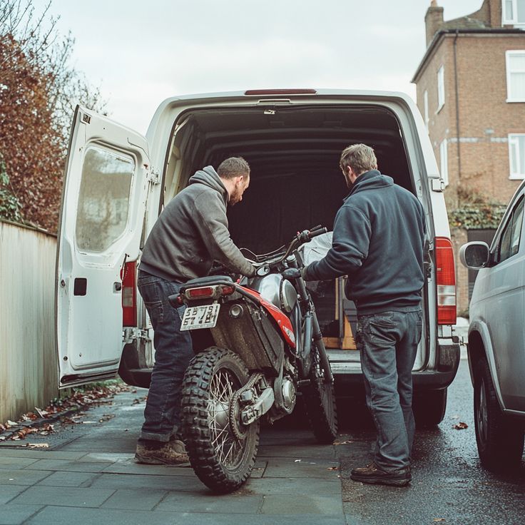 two men loading a motorcycle into the back of a white van